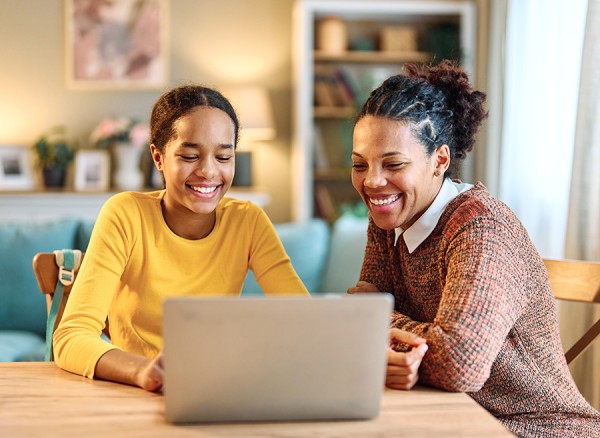 Mother and daughter sit and use a computer connected to fiber internet while smiling.