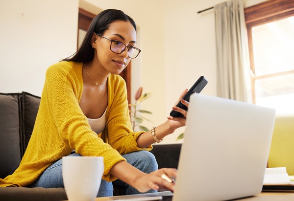 Woman sits of computer connected to internet while simultaneously using a cell phone.