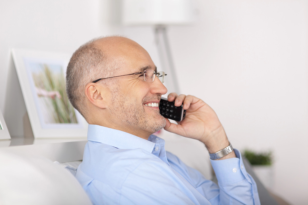 Elderly man sitting on couch with side view smiling and talking on phone.