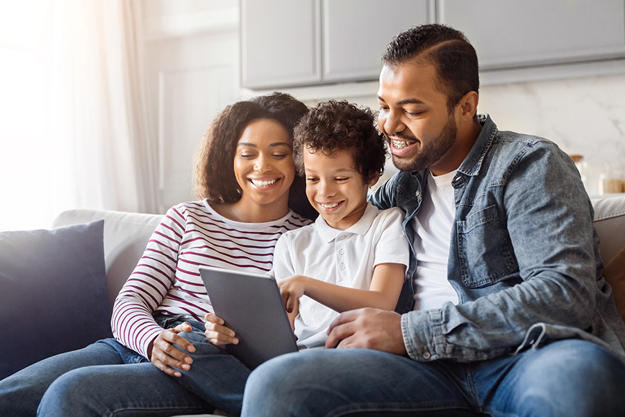 Family sits on couch using tablet.